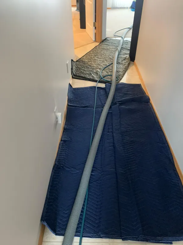 A hallway with padded blue blankets laid over the hard floor and the cleaning hoses running along them